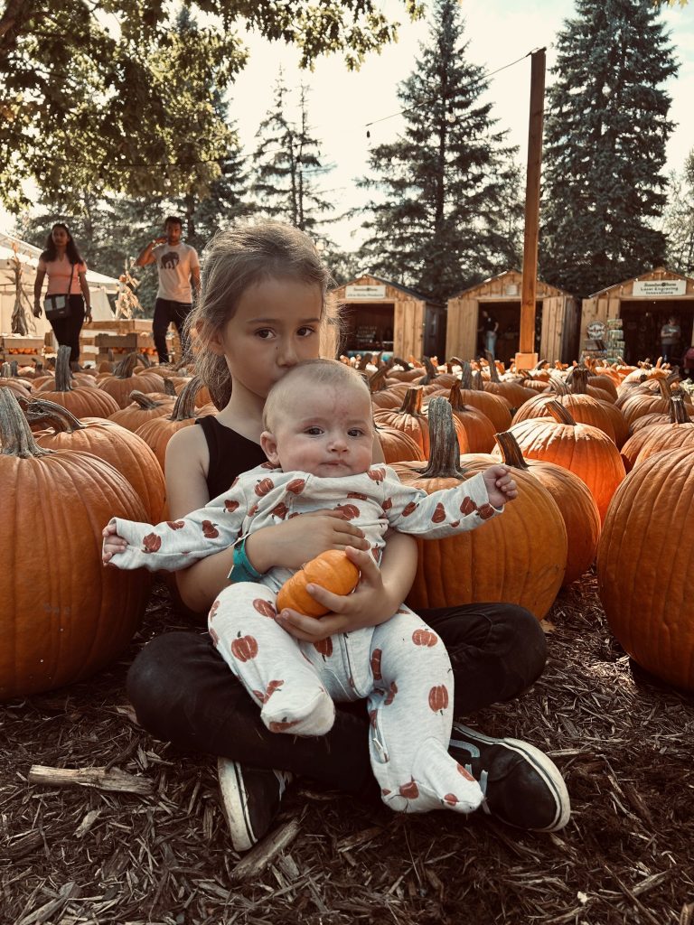 Photo of young girl holding a baby surrounded by pumkins